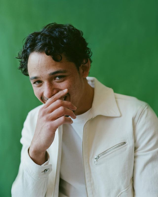 Anthony Ramos smiling in a white t-shirt and white jacket.